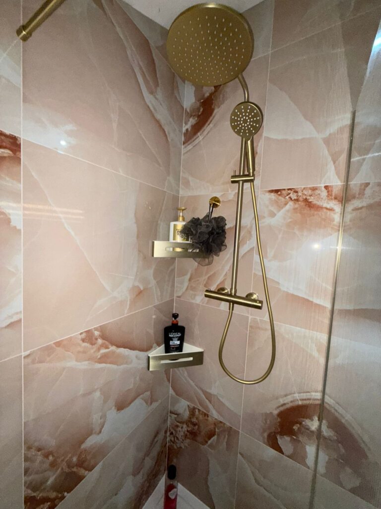 Close-up of a modern shower enclosure featuring rose gold fixtures and pink onyx-style wall tiles.