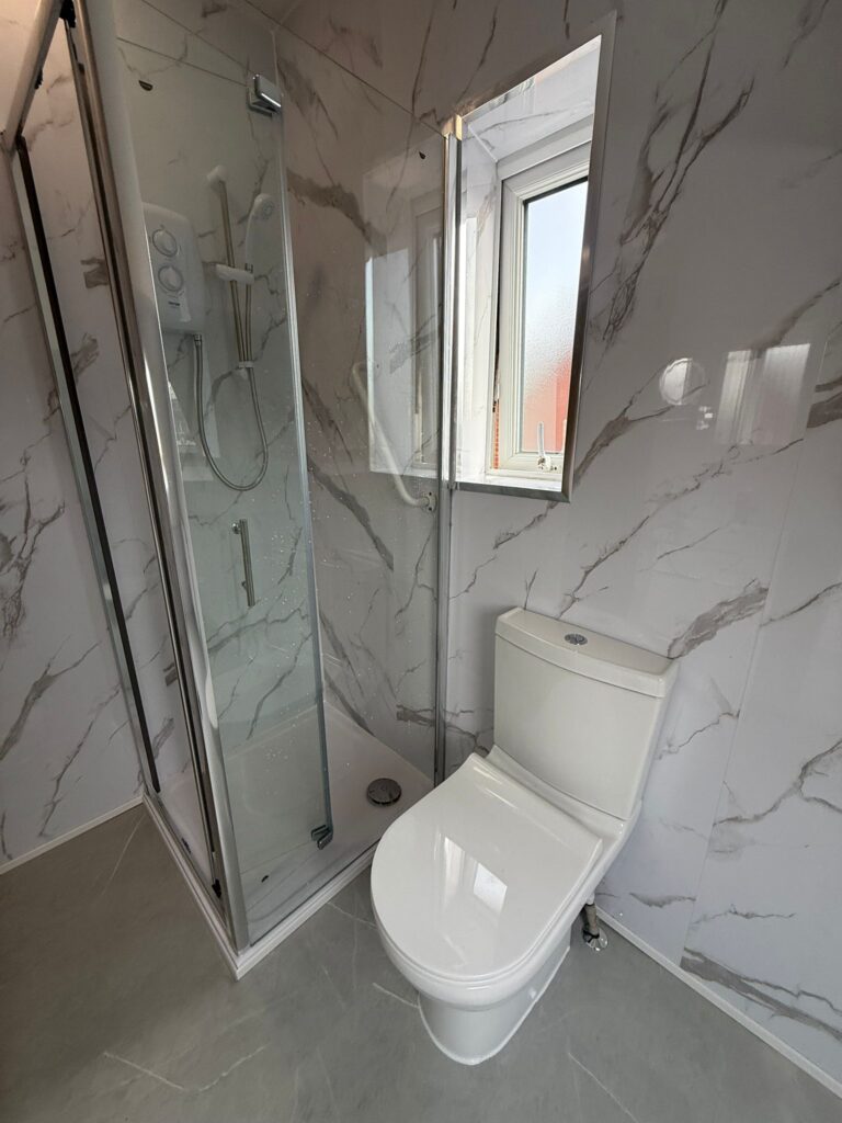Modern bathroom renovation featuring a white toilet and a corner shower enclosure with marble-effect wall panels.