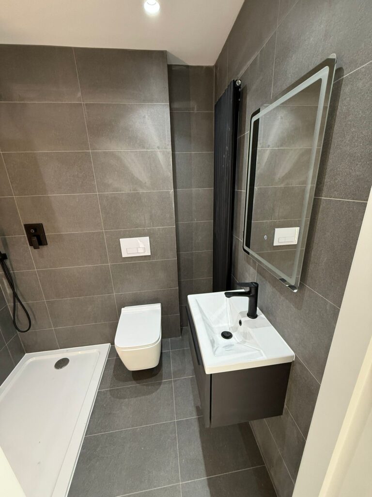 Modern bathroom renovation featuring large grey wall tiles, a wall-hung toilet, and a black vertical radiator.